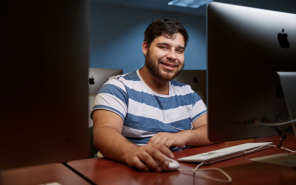 A UWF students smiles while sitting at a Mac computer lab workstation.