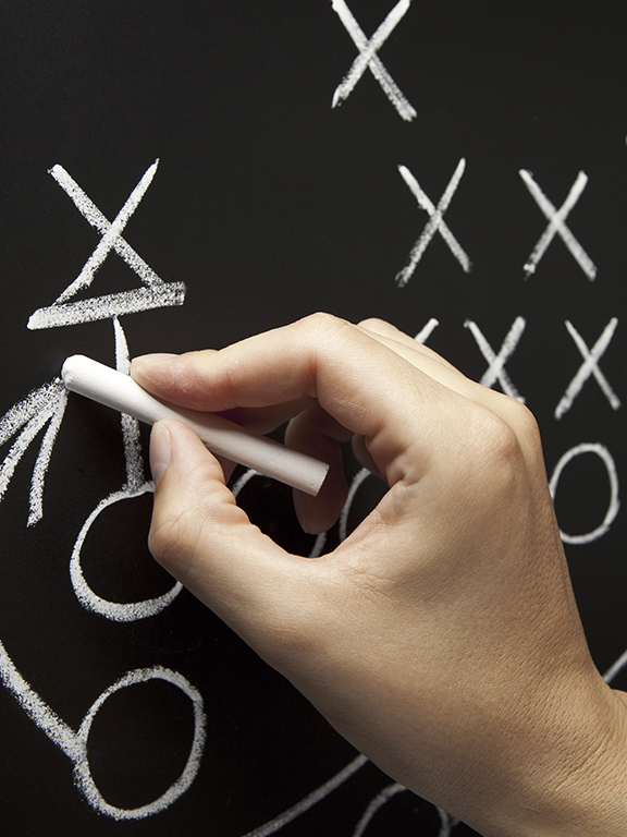 Man drawing a game strategy with white chalk on a blackboard.