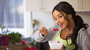A smiling lady is eating a bowl of strawberries.