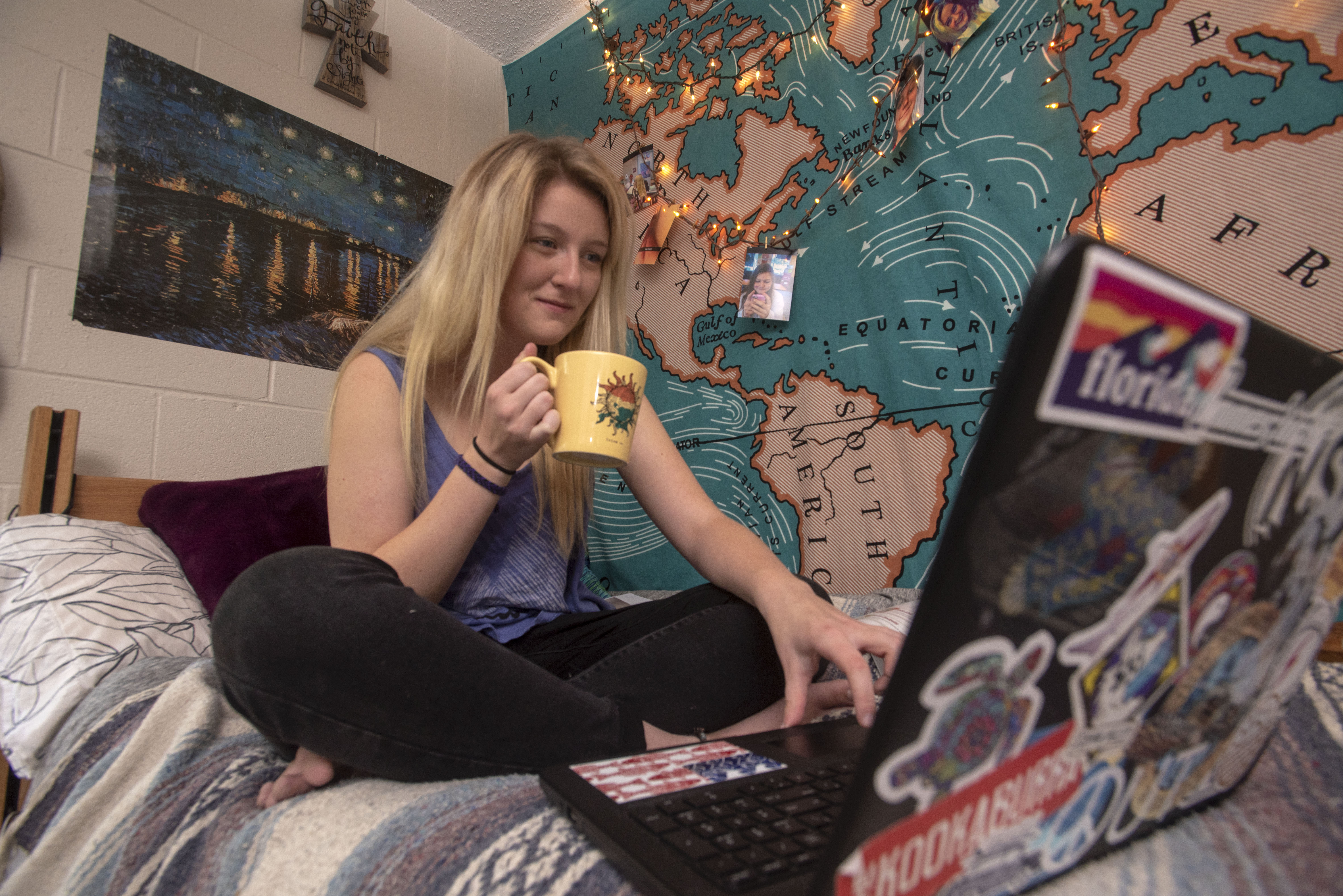 student using laptop on bed with mug