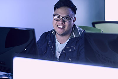 A UWF student smiles while using a computer in a dimly lit classroom.