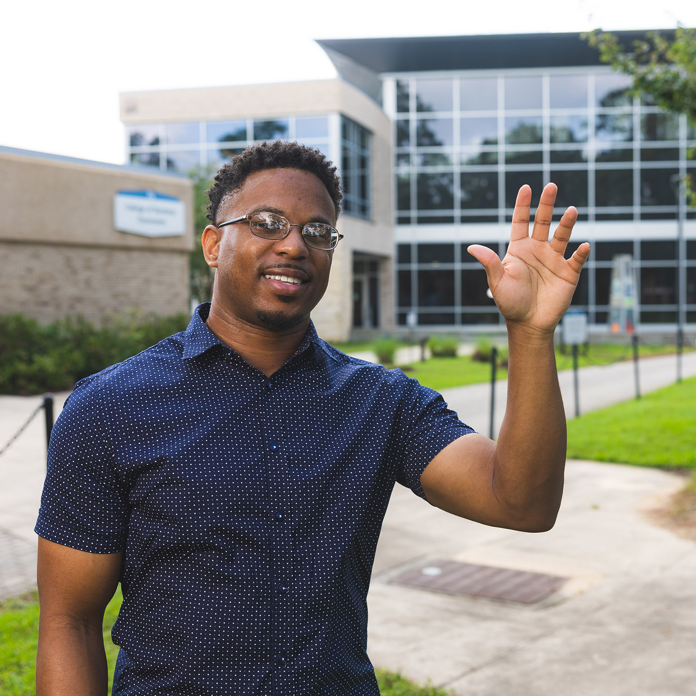 Nate Benton, Jr., smiles and waves while standing outdoors at UWF.