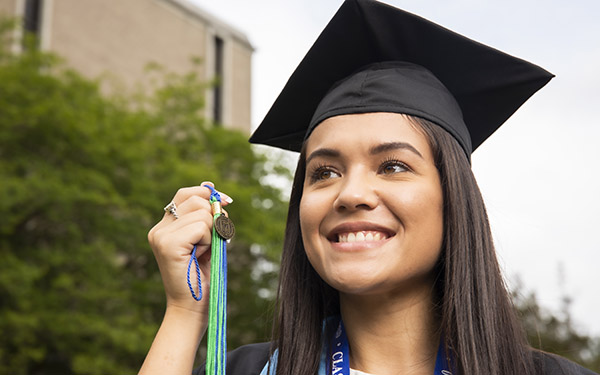 A UWF graduate in cap and gown holds up a tassel.