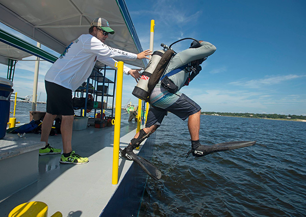 A UWF staff member in a ball cap and white long sleeve shirt spots a student diver as they enter the water
