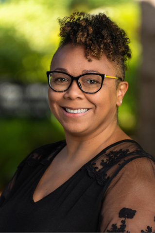 Staff member wearing a black shirt in front of greenery.