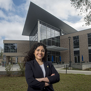 Student in professional attire smiling at camera while outdoors standing in front a of building.