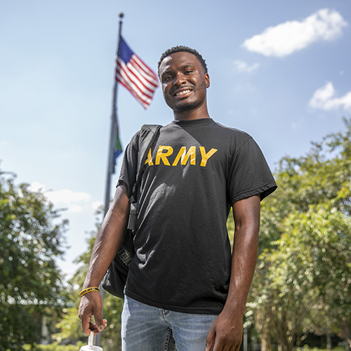 Army veteran posing in front of the US flag on a flagpole on the Pensacola campus
