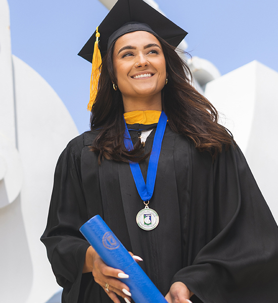 A UWF graduate wearing cap and gown and smiling