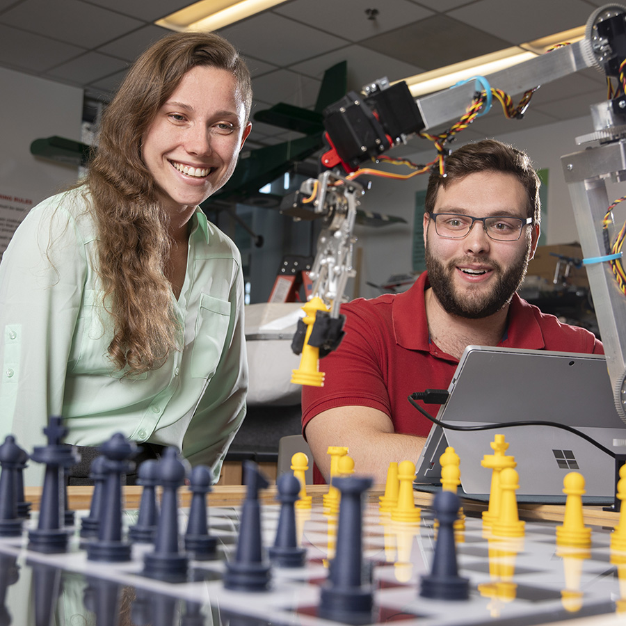 Two students using a robot arm to play chess.