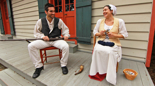 A male and female historical reenactor are sitting in chairs on the porch of the Lavalle House.