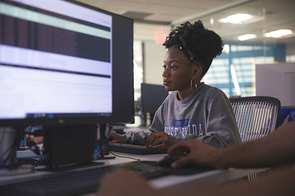 A student using a computer with a screen of a different computer present in the foreground.