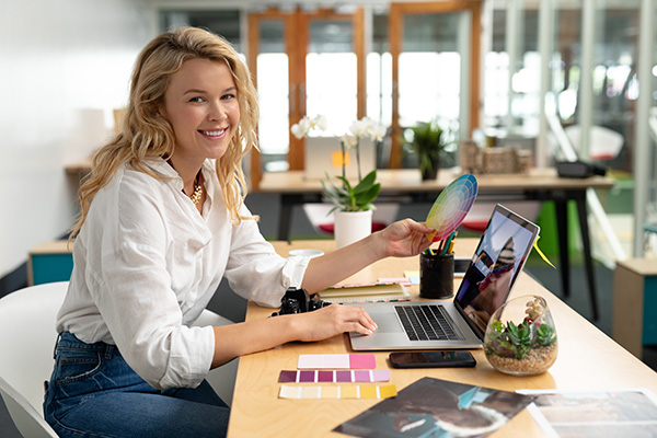 Photographer using a laptop at a desk while working with color swatches.